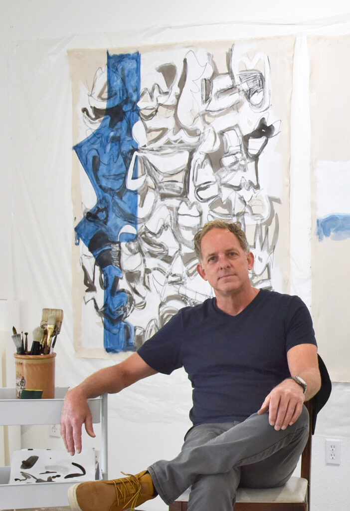 Toby Hill sitting in front of his artwork