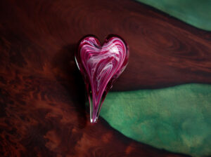 Evoking gratitude, this is an image of a hand-blown glass heart paperweight on an old growth redwood river table