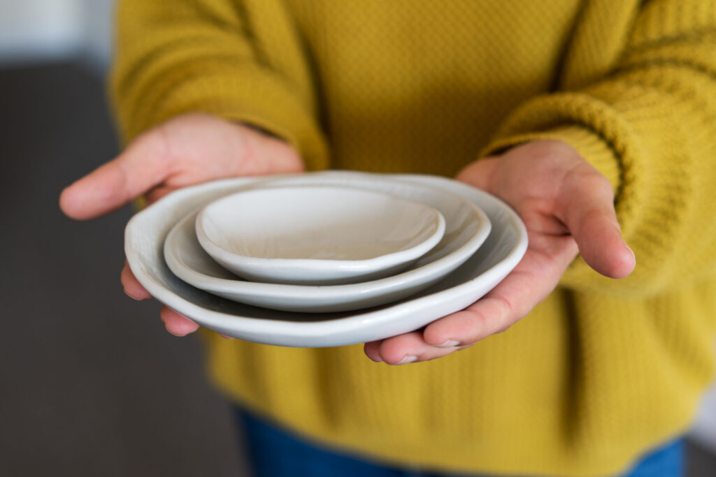 A woman in a yellow sweater is holding a set of nested white ceramic bowl in a gesture of giving.